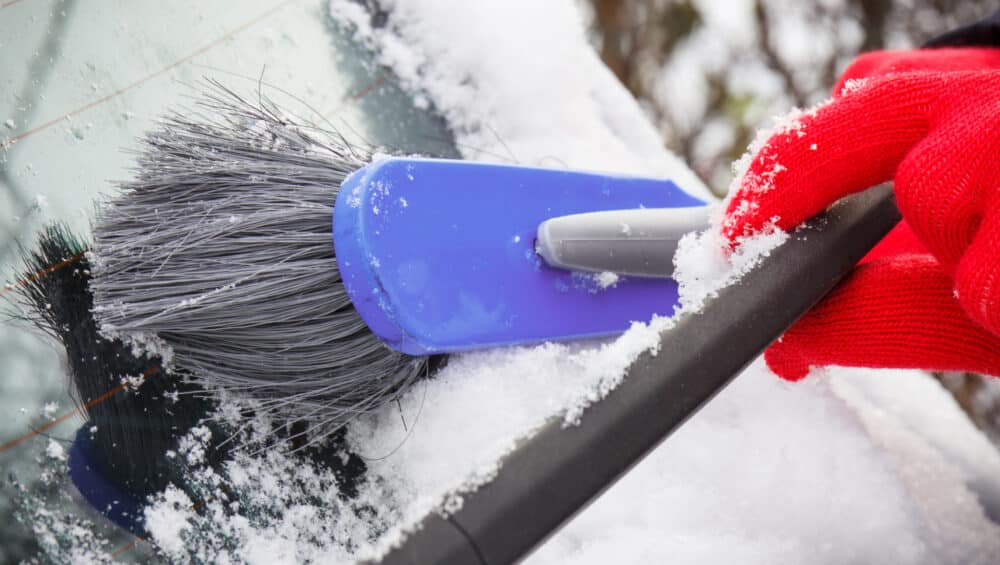 Hand of woman using brush and remove snow from car and windscreen