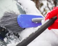 Hand of woman using brush and remove snow from car and windscreen