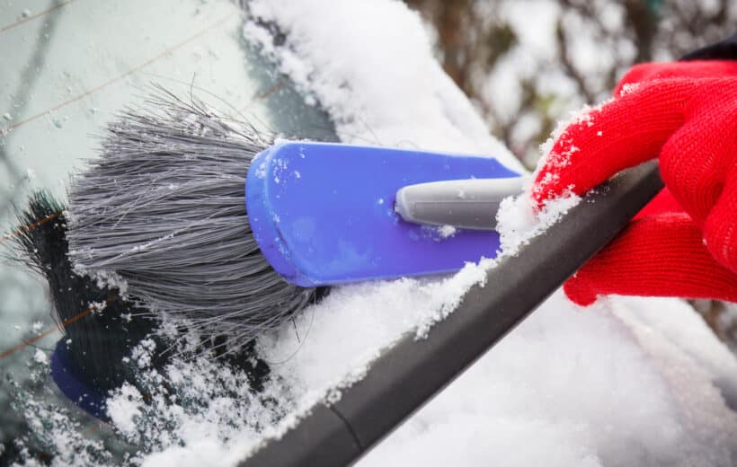 Hand of woman using brush and remove snow from car and windscreen